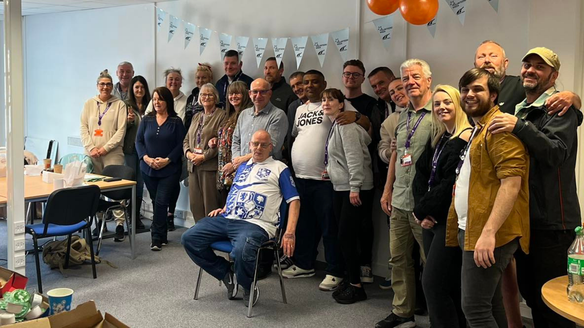 Wirral Ways Volunteers Celebrating Volunteers Week (16:9) A large group of Wirral Ways volunteers standing together in a decorated room with bunting and balloons, smiling for a group photo during Volunteers Week celebrations.